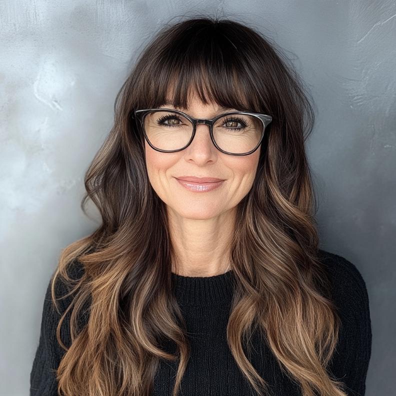 Blunt bangs paired with long, flowing layers, creating a bold yet feminine look for women over 40 with glasses.